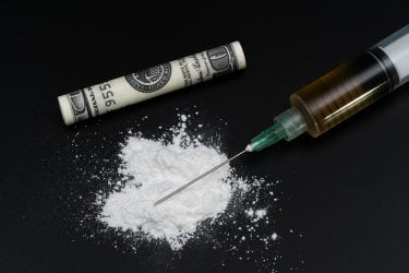 pile of white powder, a syringe filled with brown liquid and a rolled up dollar bill - cocaine use paraphanalia